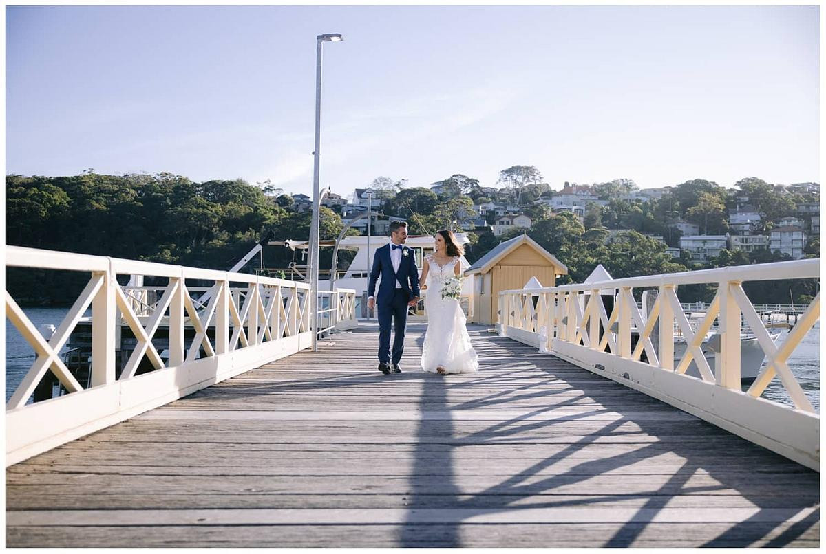 A candid wedding photo of the bride and groom walking on the pier in front of Ripples Chowder Bay on their way to Sergeants Mess Mosman.